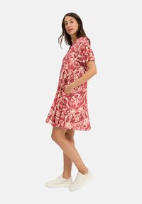 Red and cream patterned dress with short sleeves and pockets, made of lightweight fabric, falling above the knee, paired with white sneakers.