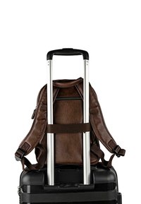 Mochila de cuero marrón asegurada sobre una maleta rígida negra, con mango extensible de aluminio y correas ajustables.