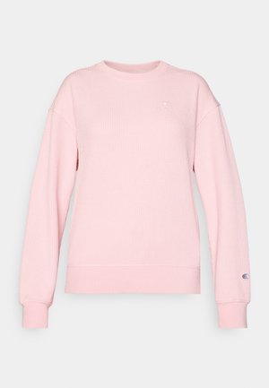 Rosa ribbestrikket genser med lange ermer, rund halslinje og logoemblem på brystet og mansjetten. Myk tekstur, tettsittende i midjen.