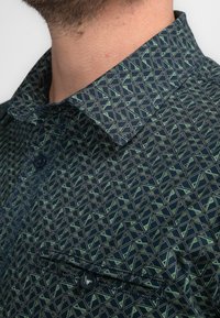 Navy button-up shirt met een geometrisch patroon in groen. Heeft een puntkraag, een borstzak en een gestructureerde stof.