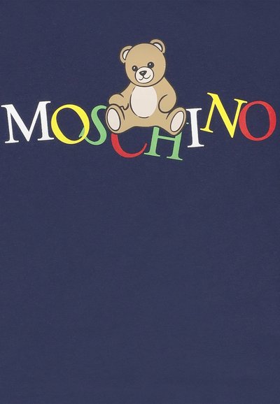 Orsetto marrone seduto sopra lettere colorate che formano la parola "MOSCHINO" su uno sfondo blu scuro.