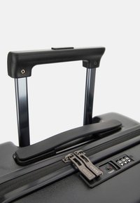 Black hard-shell suitcase with a retractable handle, dual zippers with a logo, combination lock, and glossy finish.