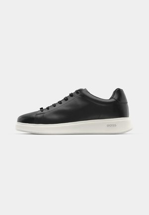 Tenis din piele neagră cu talpă albă texturată, vârf rotund și șase găuri pentru șireturi. Prezintă o marcă subtilă pe călcâi. Finisaj neted în ansamblu.