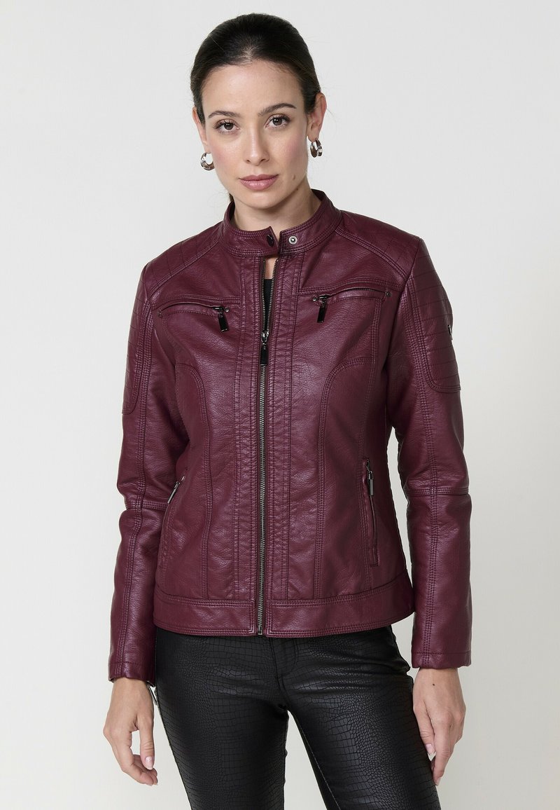 Veste en cuir bordeaux avec un col montant, des poches zippées et des accents matelassés aux épaules. Texture lisse et coupe ajustée.