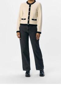 Krämfärgad kardigan med marinblå detaljer, utrustad med två framfickor och svarta knappar. Kombinerad med högmidjade mörka jeans och svarta stövlar.
