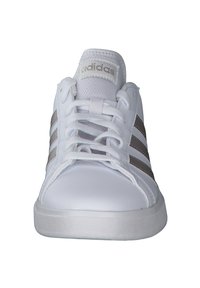 Baskets blanches en matériau synthétique lisse, arborant trois rayures métalliques argentées, un laçage traditionnel et une semelle en caoutchouc texturé.