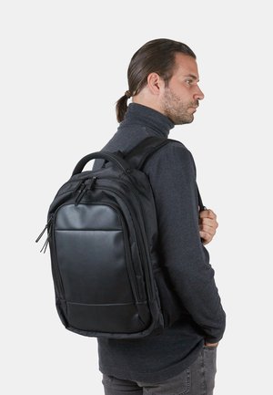 Black backpack made of durable fabric, featuring a smooth synthetic front panel, zippers, and padded straps. Mesh side pocket visible.