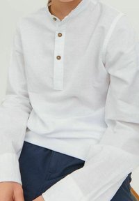 Biała koszula z długim rękawem i kołnierzykiem mandaryńskim, z zapięciem na guziki z trzema brązowymi guzikami, wykonana z teksturowanej tkaniny.