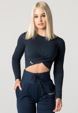 Mørkeblå langærmet crop top med snoet frontdesign, parret med højtaljede mørkeblå joggers med lommer og logo på benet.