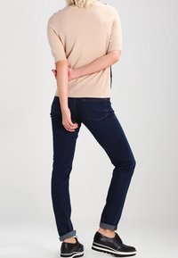 Beige, kortärmad tröja med ribbad textur, i kombination med mörkblå jeans och svarta skor med en vit platåsål.