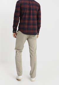 Rot-kariertes Langarmhemd in Marineblau mit Knopfmanschetten, kombiniert mit hellen khakifarbenen Hosen und weißen Sneakers. Zeigt eine lockere Passform.