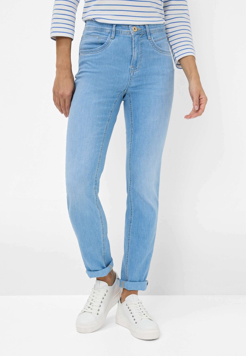 Jean en denim bleu clair avec une coupe décontractée, ourlets retroussés, poches avant et une texture lisse. Associé à des baskets blanches.