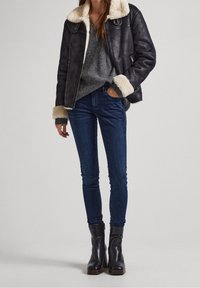 Black leather jacket with beige shearling collar, gray sweater, blue skinny jeans, and black ankle boots with a low heel.
