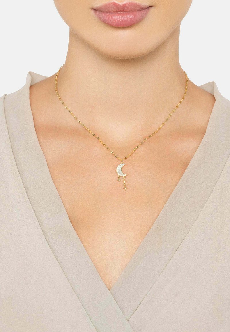 Gold necklace with a crescent moon pendant adorned with small stars, featuring a delicate chain and a smooth texture, worn over a light blouse.