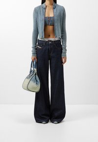 Cárdigan de canalé azul claro, corto, encima de un top corto de flores azules. Pantalones vaqueros anchos oscuros y un bolso azul texturizado con un acabado degradado.
