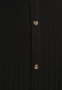 Nahaufnahme eines schwarzen, gerippten Stoffes mit zwei glänzenden braunen Knöpfen, die vertikal auf einer genähten Leiste angeordnet sind.