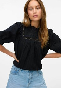 Svart blus med puffade korta ärmar, texturerad tyg, spetsdetaljer vid halsringningen och veck. Matchad med ljusblå denimshorts.