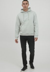 Světle šedá mikina s kapucí a přední kapsou, se šňůrkou a potištěným logem. Spárována s černými slim-fit džíny a černými teniskami.