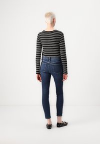 Striped black and white long-sleeve shirt paired with blue skinny jeans featuring a high waist and back pockets. Footwear includes black flats.
