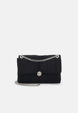Pochette noire matelassée avec fermoir rotatif argenté et bandoulière chaîne argentée sur fond gris clair uni.