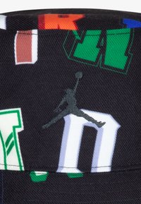 Svart tøyhatt med flerfargede trykte bokstaver og svart brodert Jumpman-logo. Designet inkluderer forskjellige dristige grafiske aksenter.