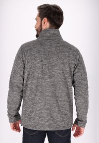 Grå texturerad pullover med hög krage och långa ärmar, tillverkad av ett mjukt tyg. Bakifrån syns en platt nederkant och detaljerad sömnad.