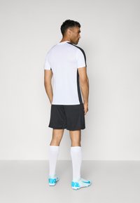 Sportlik riietus, mis sisaldab valget ja musta lühikeste varrukatega särki, musti šortse, valgeid sokke ja siniseid ketsid, millel on "NIKE" brändimisega.