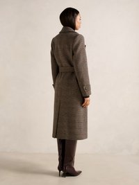 Cappotto di lana a quadri marrone con vita cinturata, colletto a scollo e tasche laterali, abbinato a stivali lucidi bordeaux al ginocchio.