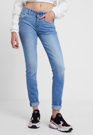 Jasnoniebieskie, wąskie, podwinięte dżinsy noszone z białym krótkim swetrem i czarno-różowymi butami Adidas.