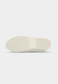 Semelle d'une basket blanche avec motif de bande de roulement crantée horizontale, montrant les sections avant et talon sur un fond clair uni.