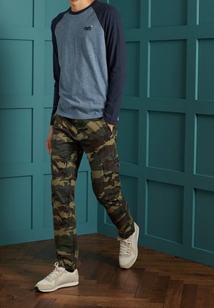 Camisa de manga larga azul y azul marino combinada con pantalones cargo camuflados y zapatillas blancas. Tejido texturizado y ajuste holgado.