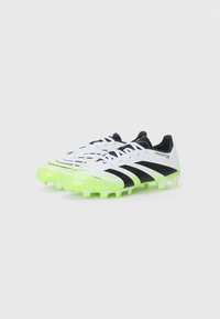 White soccer cleats with black stripes and logo, featuring a textured upper and bright green accents on the sole and toe area.