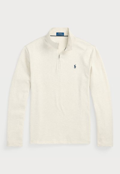 Svetlo bež dolg rokav pulover s polzadrgo. Ima majhen mornarsko modri logotip na prsih. Mehak, teksturiran material, casual fit.