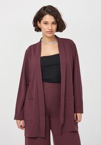 Bordowy, lekki kardigan zapinany na otwarto z długimi rękawami, dwoma przednimi kieszeniami i luźnym krojem, noszony na czarnym topie.