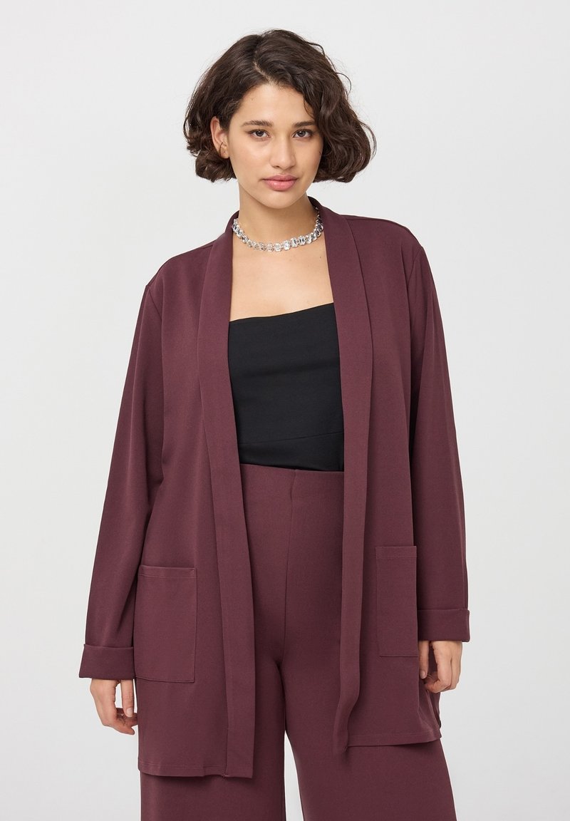 Bordowy, lekki kardigan zapinany na otwarto z długimi rękawami, dwoma przednimi kieszeniami i luźnym krojem, noszony na czarnym topie.