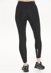 Zwarte high-waisted leggings van rekbare stof, met zijzakken en reflecterende verticale strepen op het onderbeen.