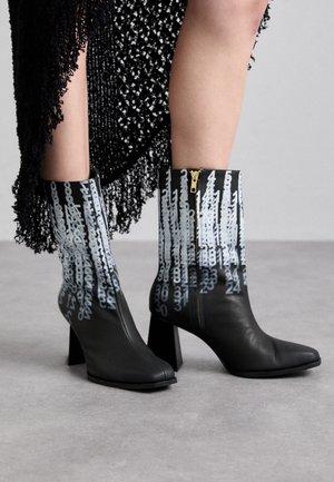 Μαύρες δερμάτινες αστράγαλοι μπότες με χοντρό τακούνι, που διαθέτουν έναν ξεχωριστό μπλε αριθμητικό σχέδιο και φερμουάρ στο πλάι για κλείσιμο.