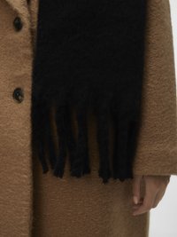 Brun tekstureret frakke med sort frynset tørklæde draperet, der viser tre knapper og en hånd med lys hud, der hviler ved siden.