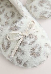 Pantoufles douces blanches et duveteuses avec des taches léopard beige et nouées avec de fines boucles en daim beige.