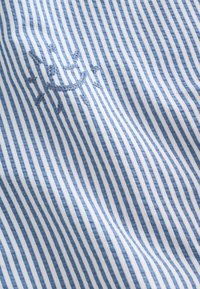Tissu rayé bleu et blanc avec un motif de soleil bleu brodé cousu sur le tissu.