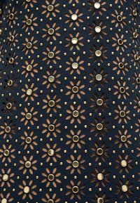 Μαύρο ύφασμα με σχέδιο από λουλουδένιες οπές, κάθε μία κεντραρισμένη με ένα χρυσό μεταλλικό καρφί και περιτριγυρισμένη από μικρές χρυσές τελείες.