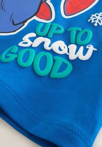 Tessuto blu con testo in rilievo "FINO A neve BUONA" in verde e bianco, parziale personaggio dei cartoni animati e un piccolo dettaglio di fiocco di neve bianco.