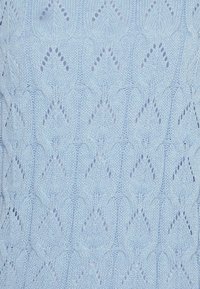 Maglione a maglia blu chiaro con motivo a rombi e dettagli traforati. La texture è liscia con forme sovrapposte ben definite.