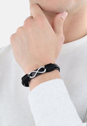 Black leather bracelet with a silver infinity symbol accent, featuring textured fabric wraps and a smooth, polished finish.