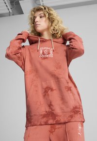 Korálová mikina s technikou tie-dye, s prednou vreckom, krémovými šnúrkami a vyšitým vzorom v strede. Mäkká tkanina s voľným strihom.