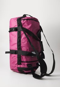 Duffle bag in vibrant pink, made of durable material, features black straps and hardware. It includes a padded shoulder strap and side buckles.