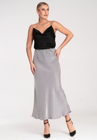 Schwarzes Satin-Cami-Top mit dünnen Trägern, kombiniert mit einem fließenden silbernen Satinkl skirt. Der Rock hat einen dezenten Glanz und einen ausgestellten Saum. Schwarze Absätze.