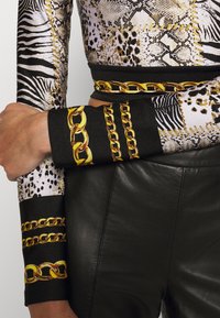 Long-sleeve top featuring animal print patterns in shades of black, brown, and cream. Black cuffs with gold chain graphics. Paired with black leather pants.