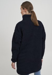 Námořnická modrá fleecová mikina s vysokým límcem, oversized střihem, texturovaným povrchem a dlouhými rukávy, dosahujícími k polovině stehna.