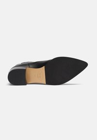 Zapato de cuero negro con punta afilada y suela plana, con una textura suave y un diseño minimalista. Etiqueta interior visible.